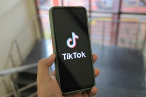 Learn to sell on tiktok seller central Hand holding a smartphone showing the TikTok app screen in an indoor setting.